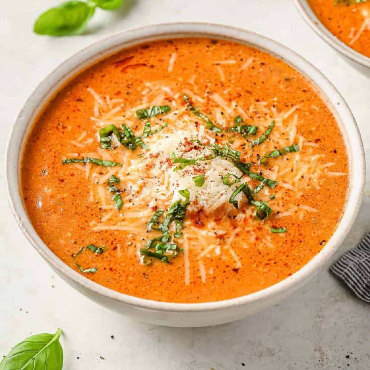 a bowl of lasagna soup, topped with ricotta cheese, parmesan cheese and fresh basil