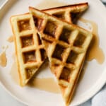 waffles on a white plate, with syrup and bacon on the side.