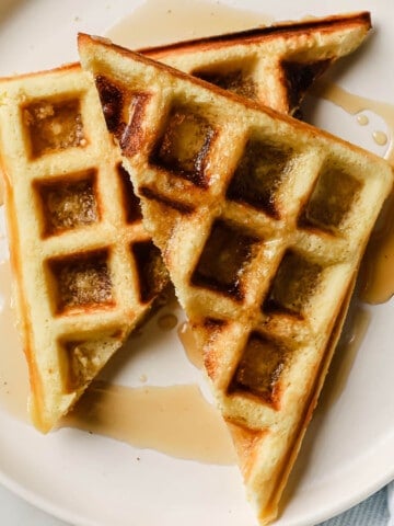 waffles on a white plate, with syrup and bacon on the side.