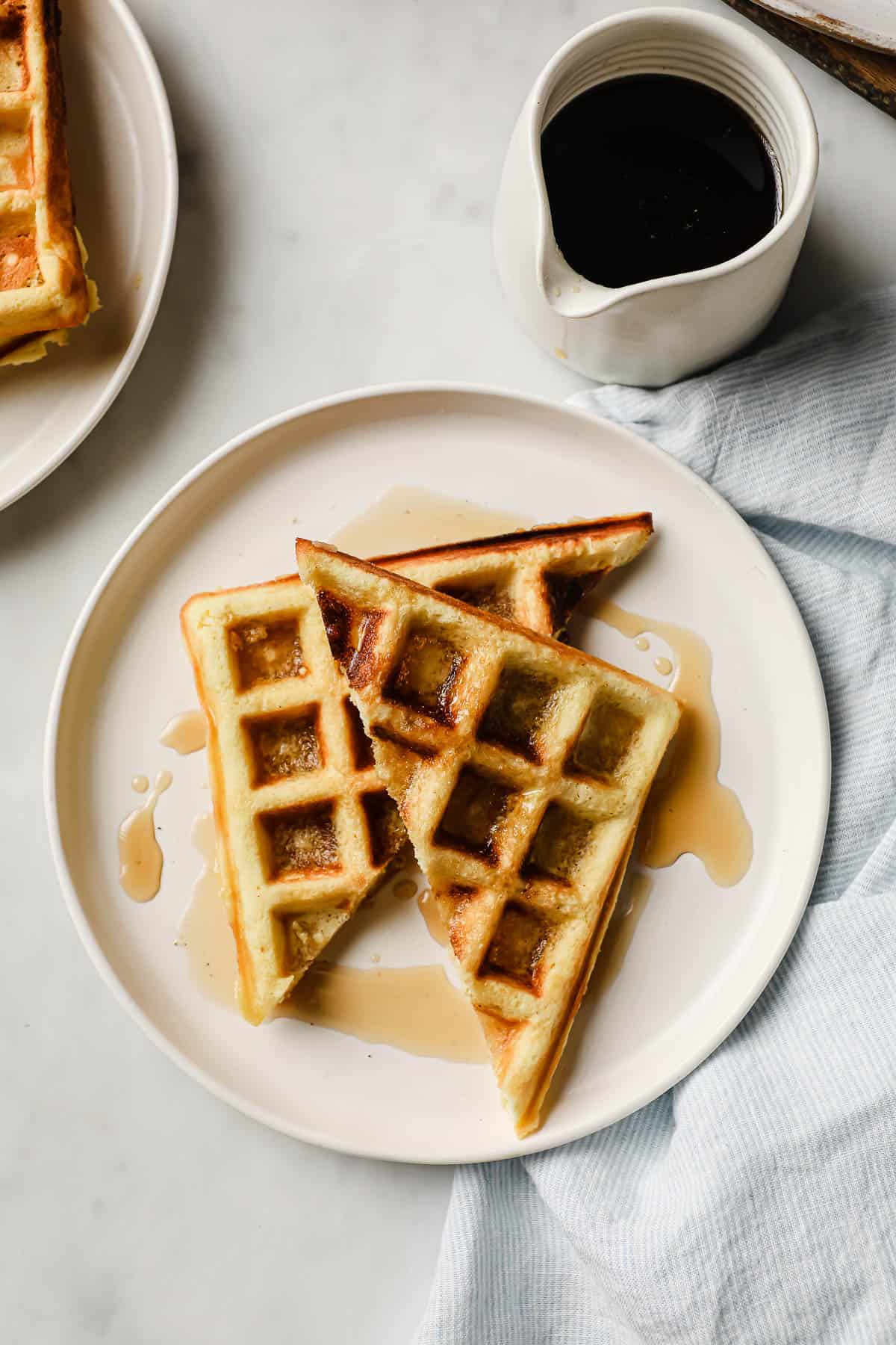 waffles on a white plate, with syrup and bacon on the side