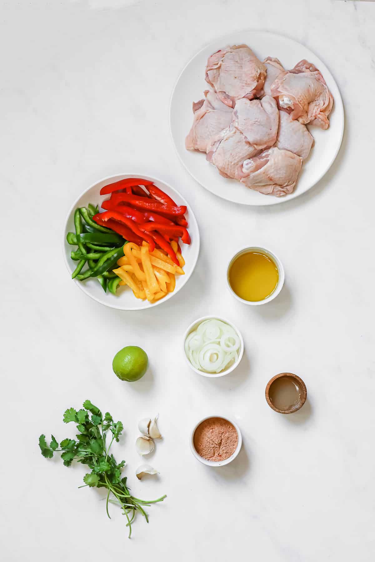 Ingredients laid out to make keto chicken fajitas - chicken, peppers, onions, seasoning, garlic, limes, cilantro