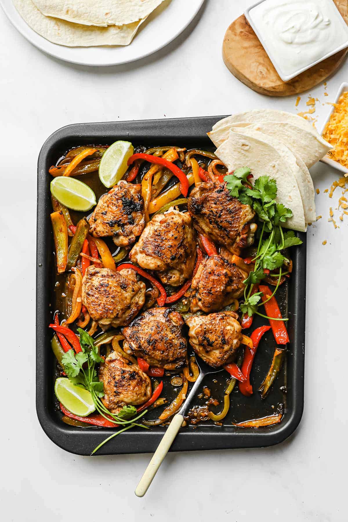 a sheet pan meal with crispy chicken thighs, peppers, onions, lime wedges, and cilantro