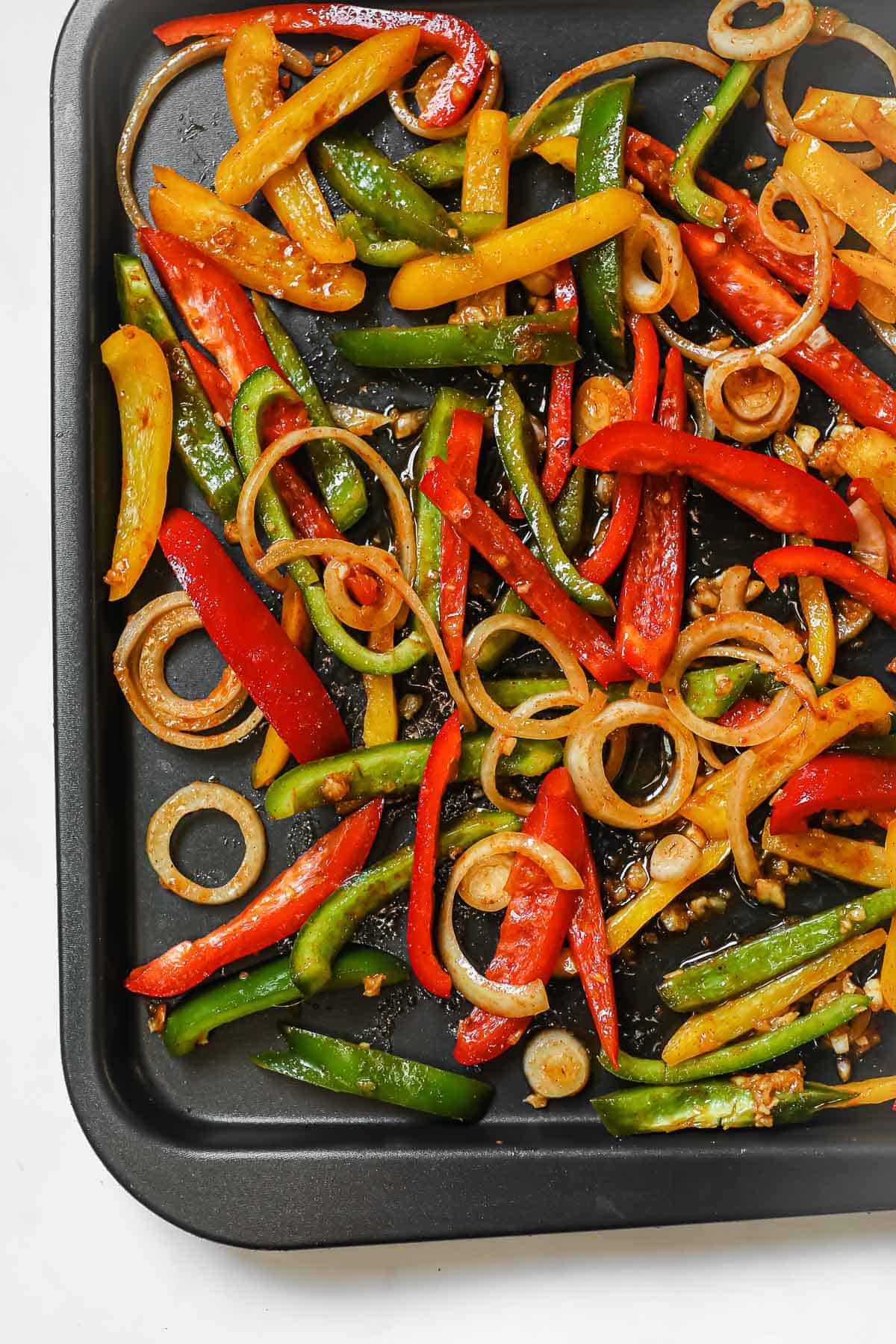 a sheet pan with sliced bell peppers and onions that have been tossed in oil and seasonings