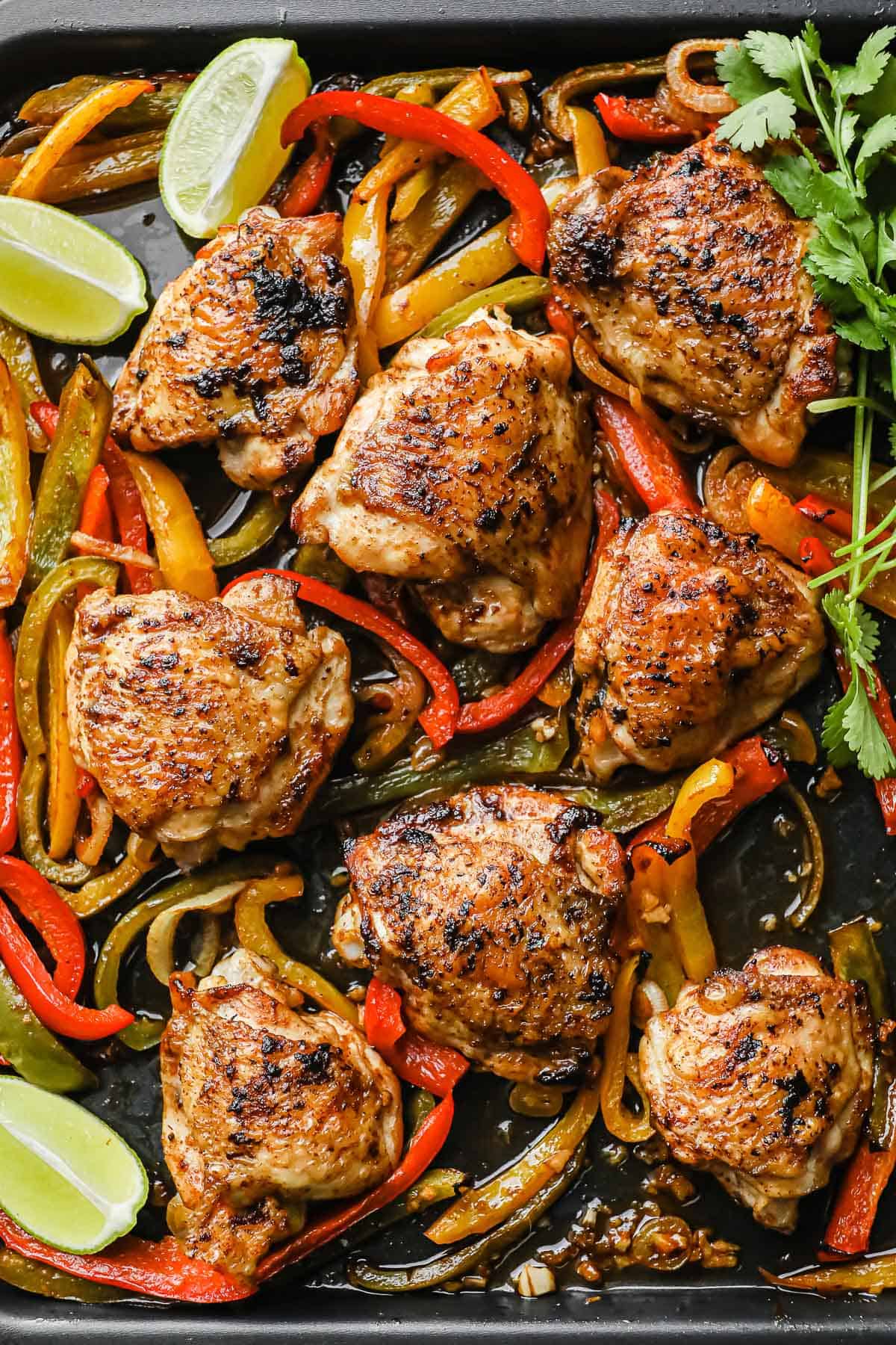 a sheet pan meal with crispy chicken thighs, peppers, onions, lime wedges, and cilantro