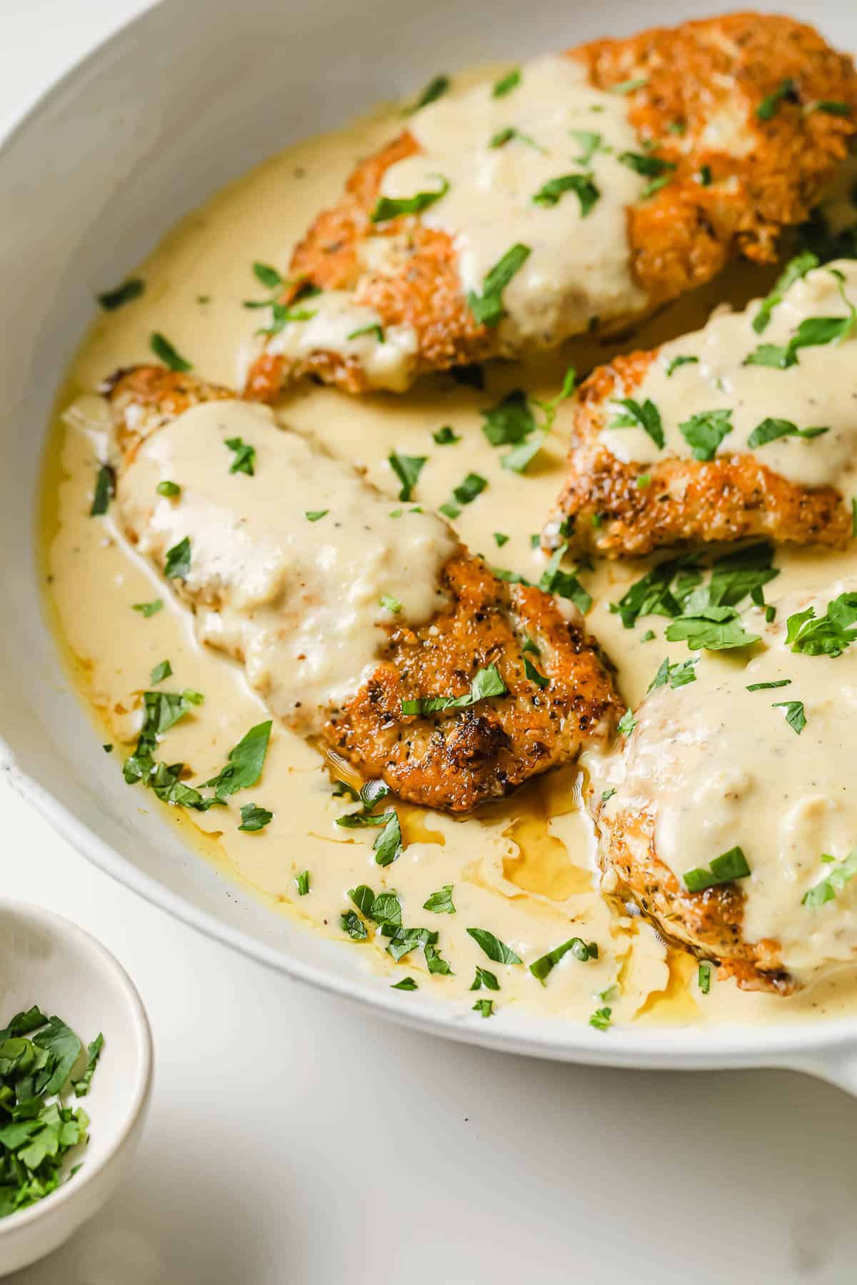a white pan with parmesan crusted chicken breasts and a velvety lemon cream sauce, garnished with parsley