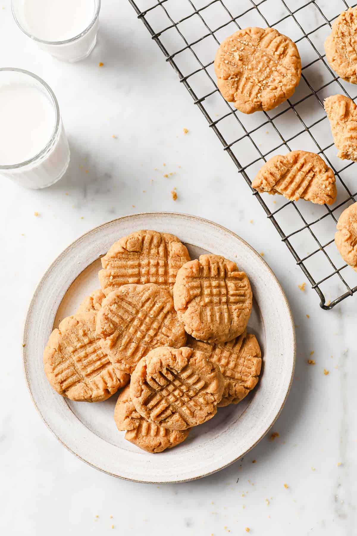 a white plate full of low carb peanut butter cookies, next to a cooling rack with cookies and milk