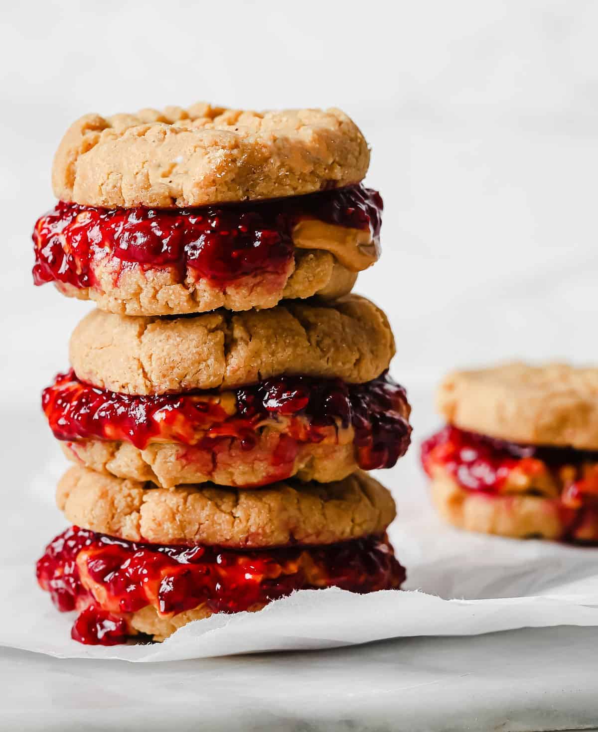 a stack of peanut butter and jelly cookie sandwiches on parchment paper