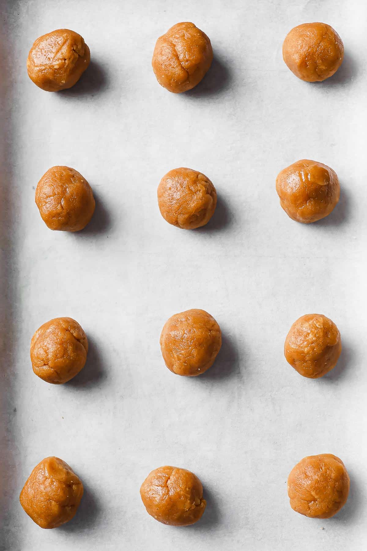a cookie sheet lined with parchment paper with dough balls of peanut butter cookie dough