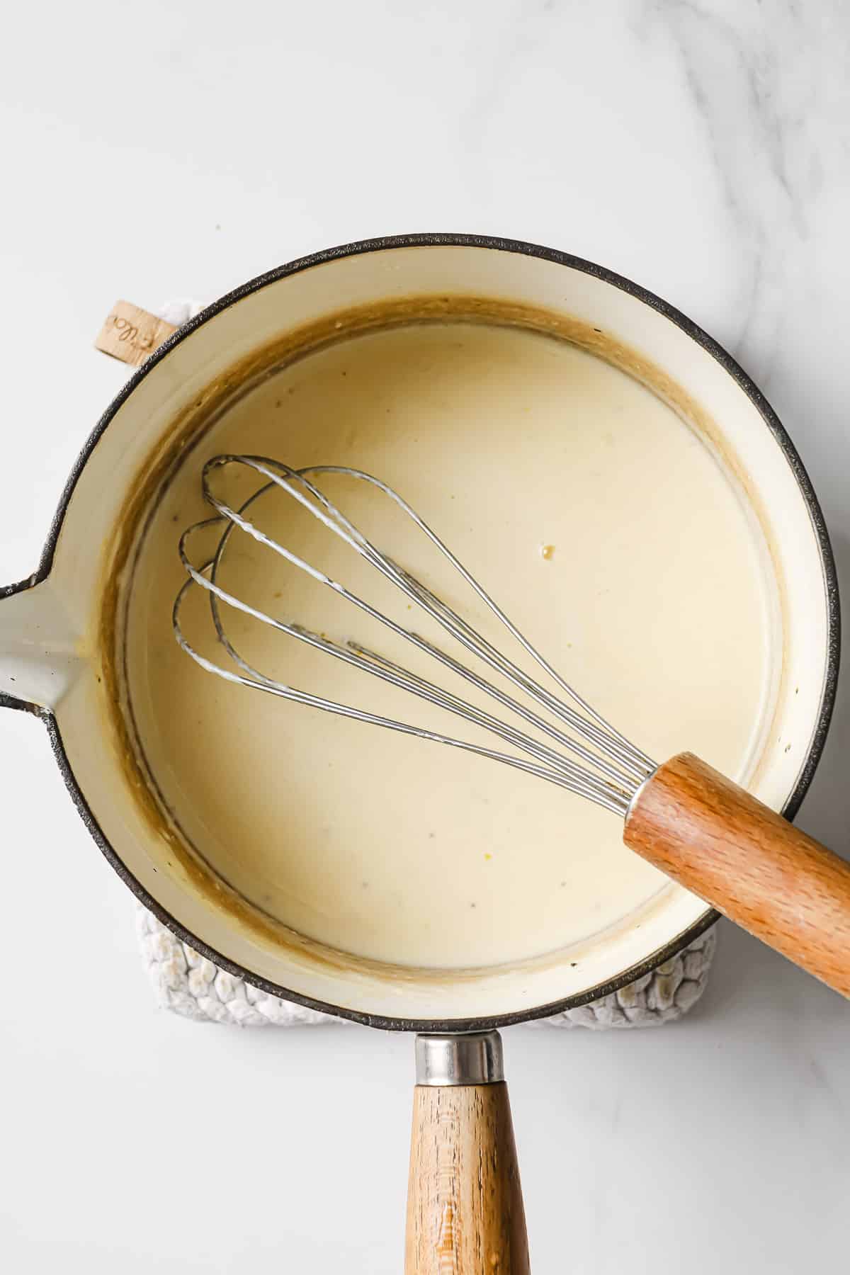 a white sauce pan with a lemon cream sauce inside and a whisk