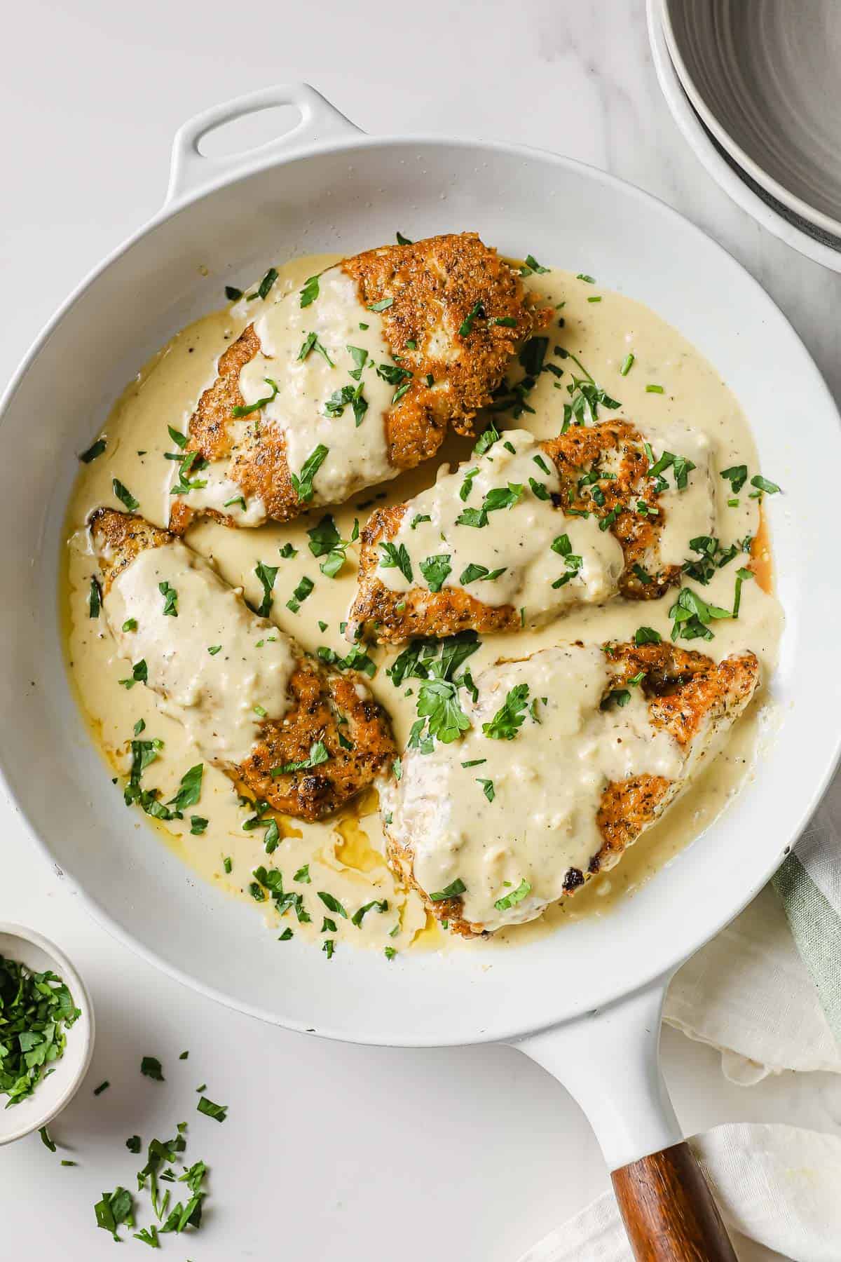 a white pan with parmesan crusted chicken breasts and a velvety lemon cream sauce, garnished with parsley