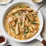 a white skillet with sautéed chicken, creamy sauce, peppers and onions, garnished with cheese and parsley