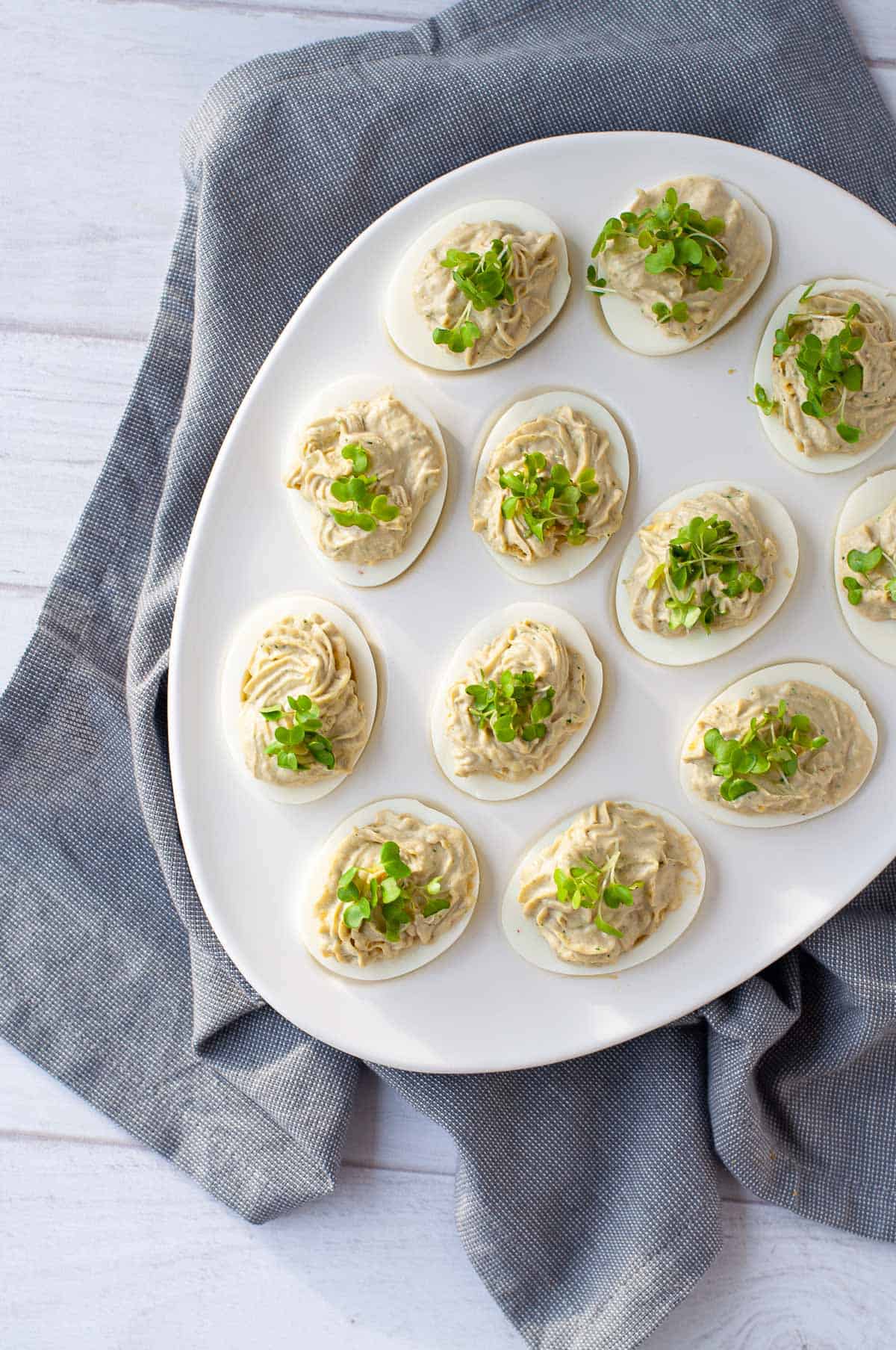 a white deviled egg holder full of pest deviled eggs, garnished with micro greens