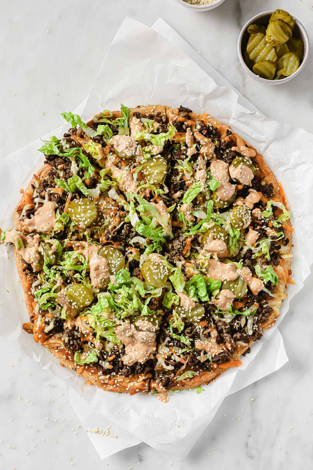parchment paper with gluten free big mac pizza, topped with beef, sauce, cheese, and lettuce.