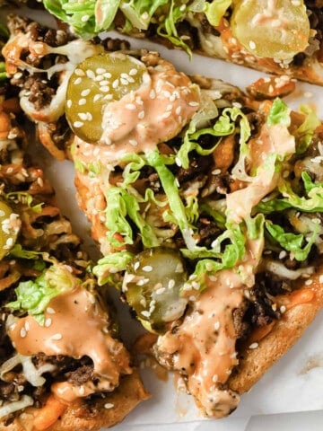 parchment paper with gluten free big mac pizza, topped with beef, sauce, cheese, and lettuce.