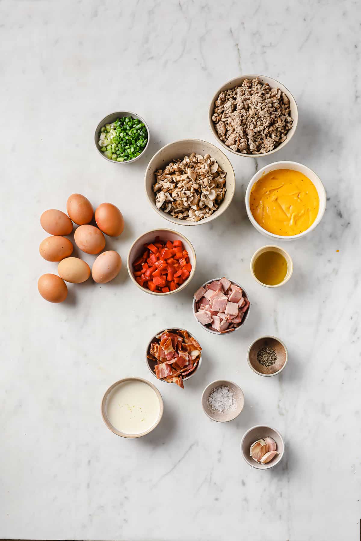 ingredients laid out to make waffle omelets - eggs, sausage, bacon, ham, onions, peppers, mushrooms and cheese sauce.