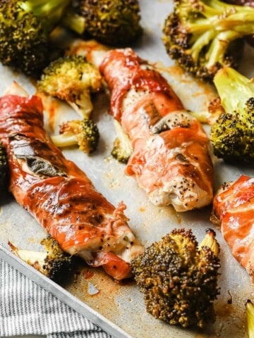 a rimmed baking sheet with roasted broccoli and prosciutto wrapped chicken.