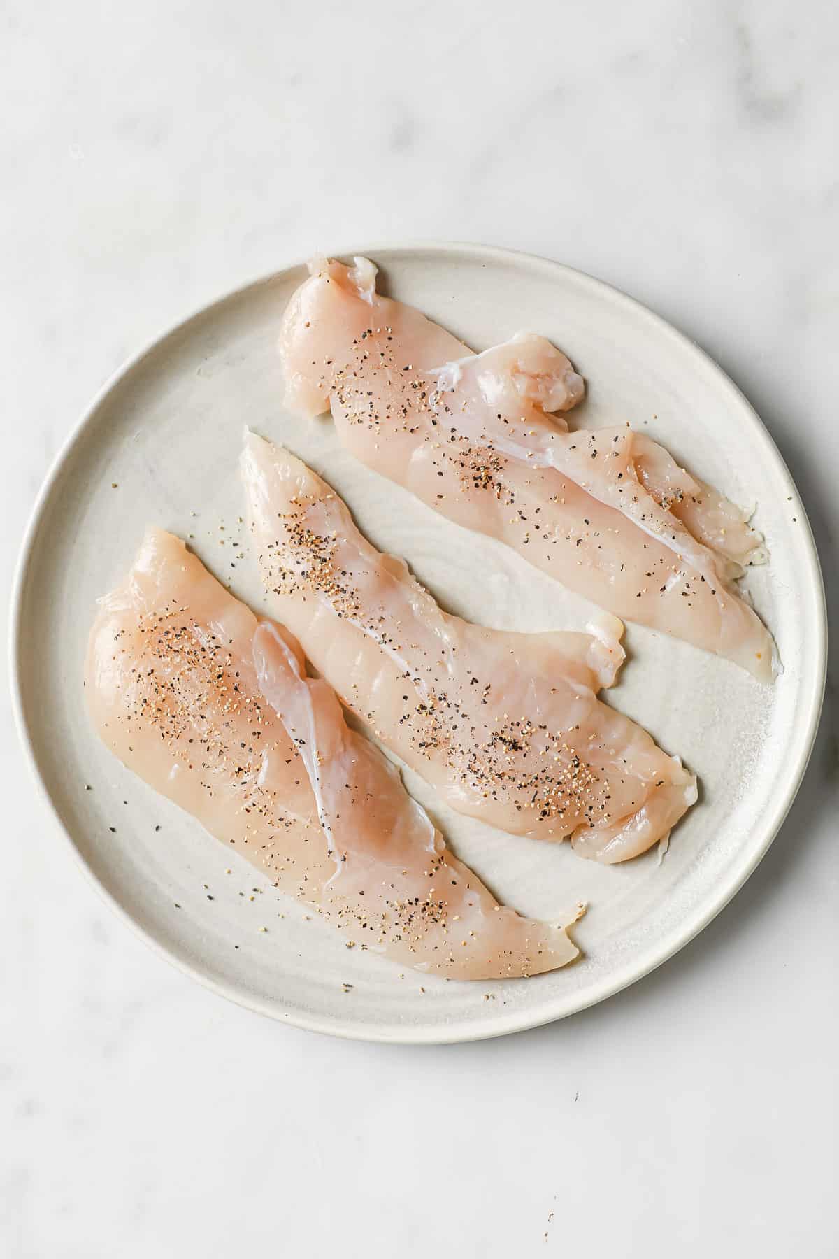 raw chicken on a plate, seasoned with sea salt and black pepper.