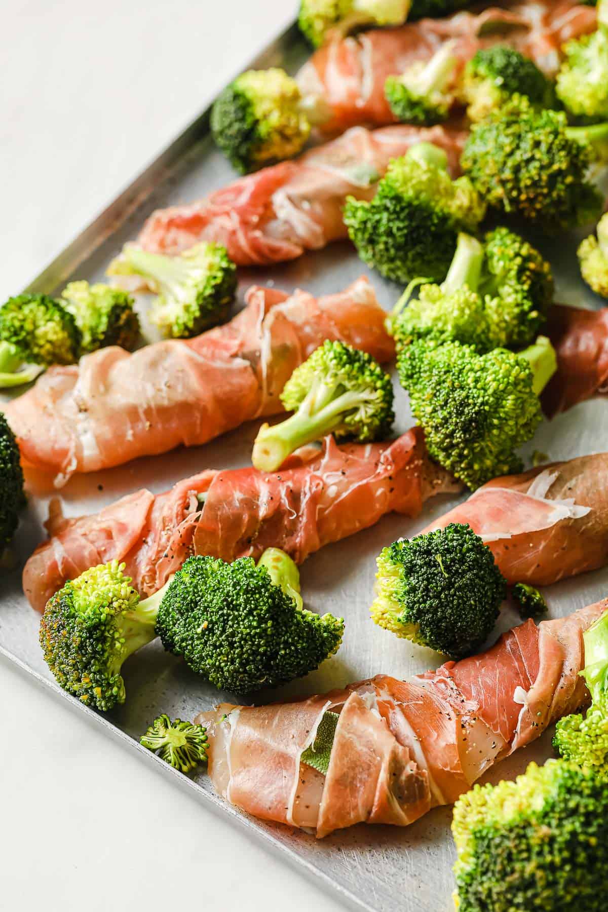 a sheet pan topped with marinated broccoli florets and chicken wrapped in prosciutto.