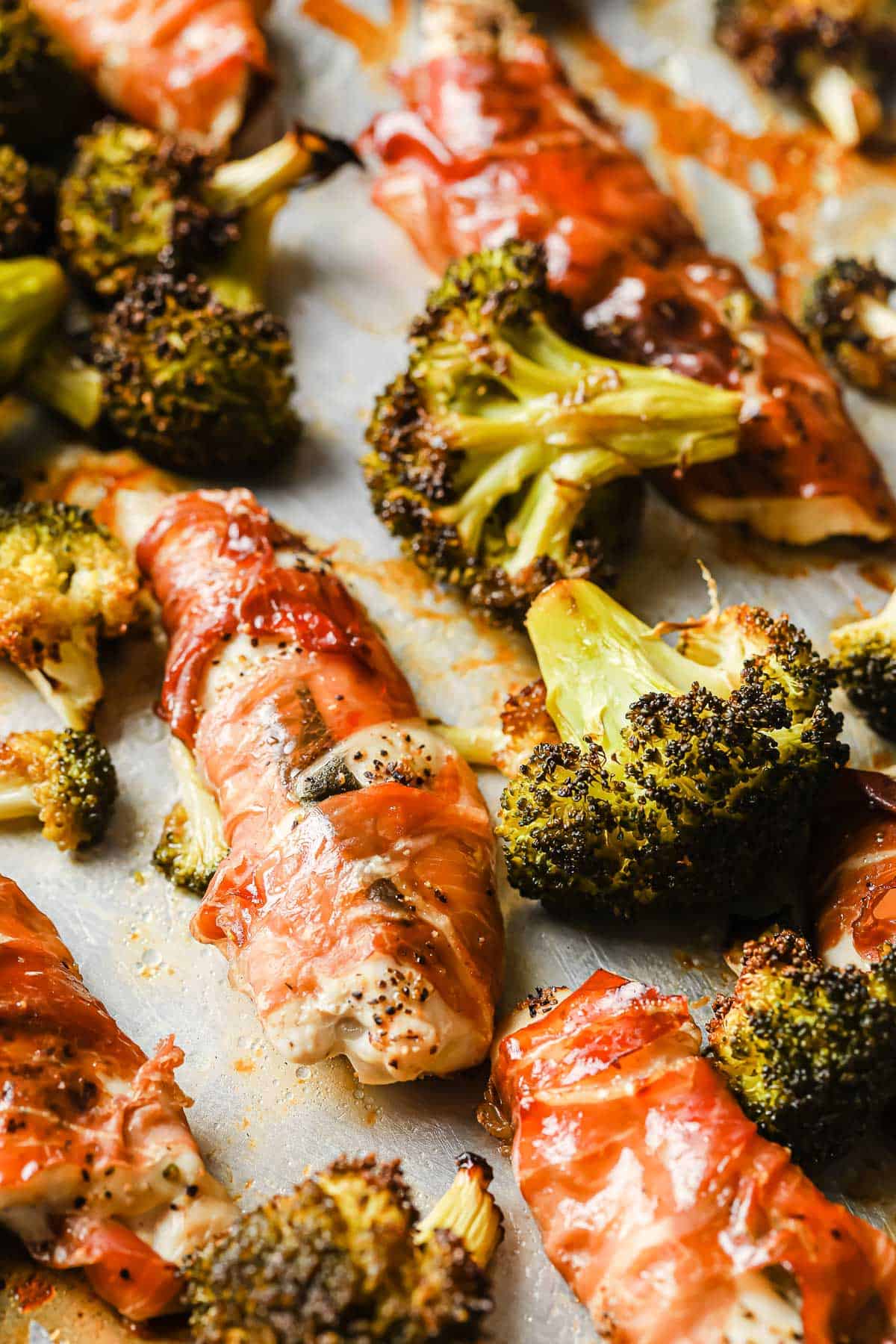 a rimmed baking sheet with roasted broccoli and prosciutto wrapped chicken.