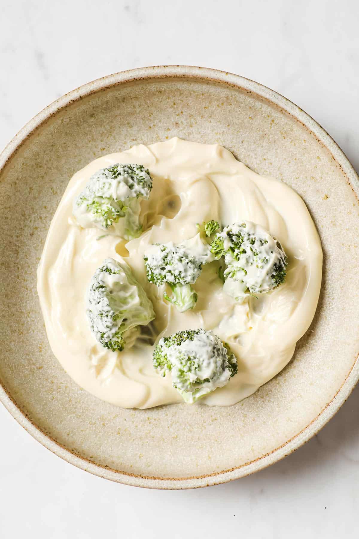 a bowl with mayo and mayo coated broccoli florets.
