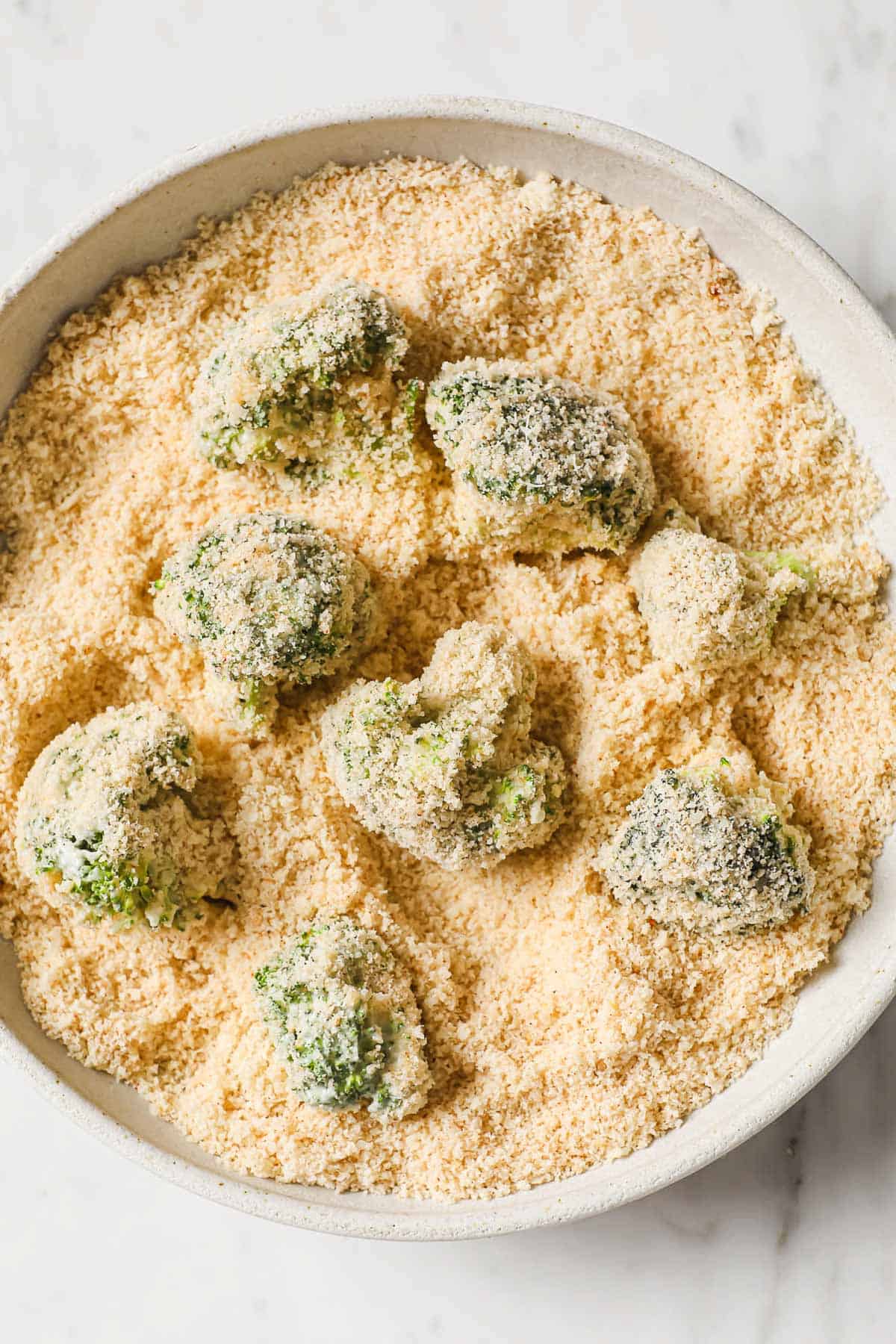 a bowl with almond flour and broccoli florets that have been coated in mayo.