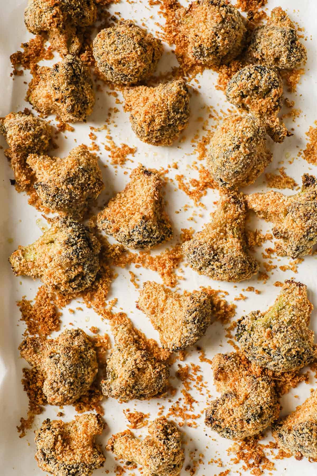 broccoli florets that have been coated in mayo and then rolled in a low carb breading and placed on a parchment lined sheet pan.