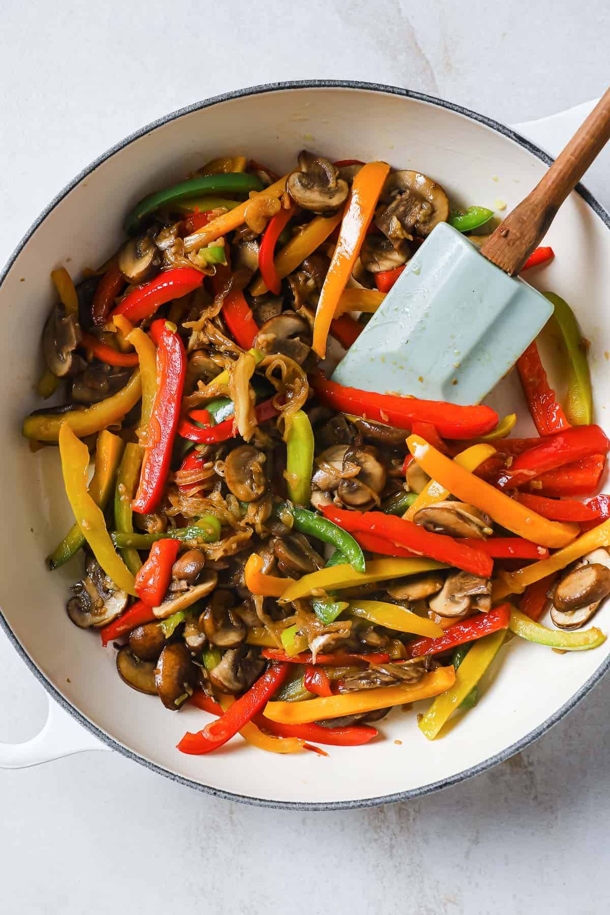a cast iron skillet with sautéed mushrooms, garlic, peppers, and onions being cooked with a rubber spatula.