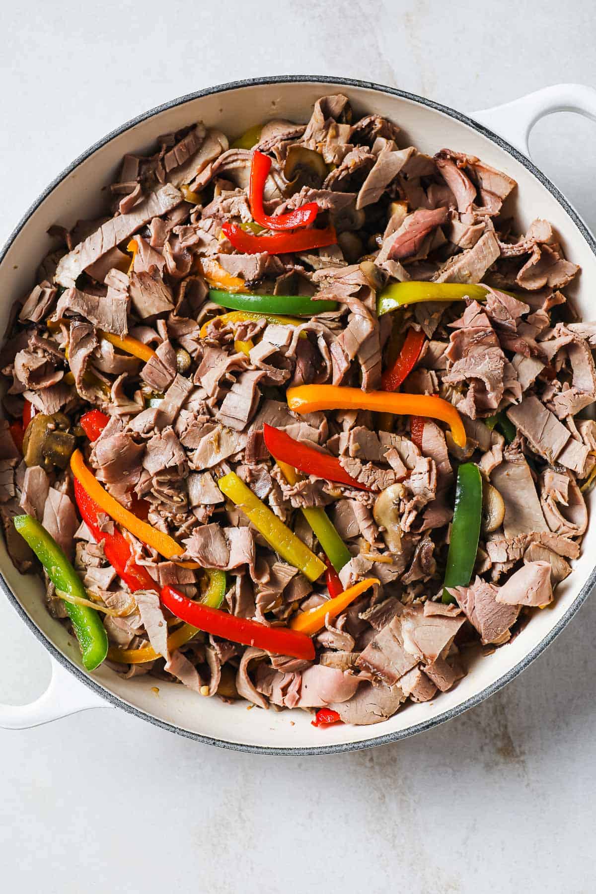 a cast iron skillet with sautéed roast beef, mushrooms, garlic, peppers, and onions