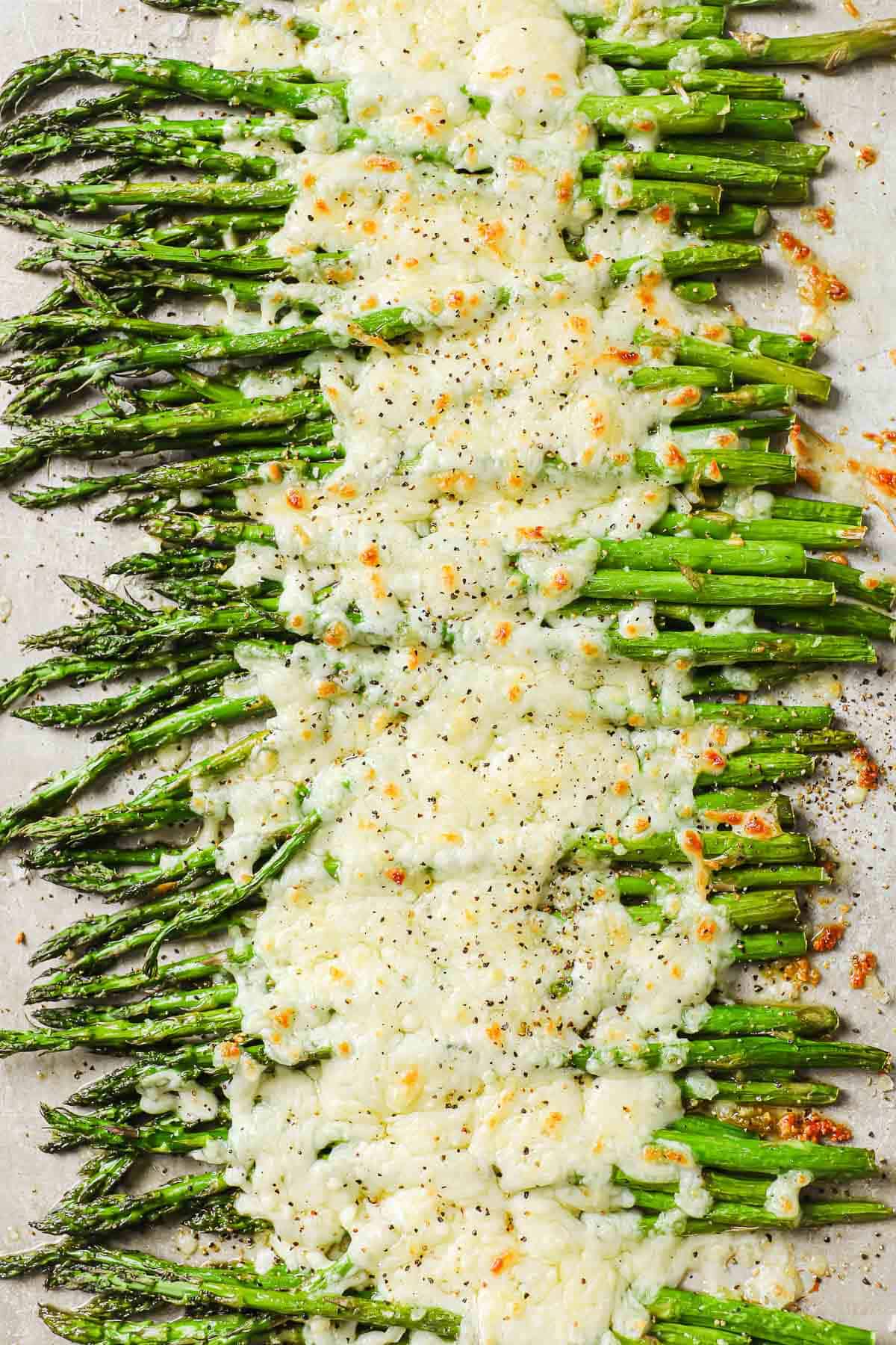 a baking sheet lined with parchment paper, full of roasted asparagus, garlic and melted cheese.