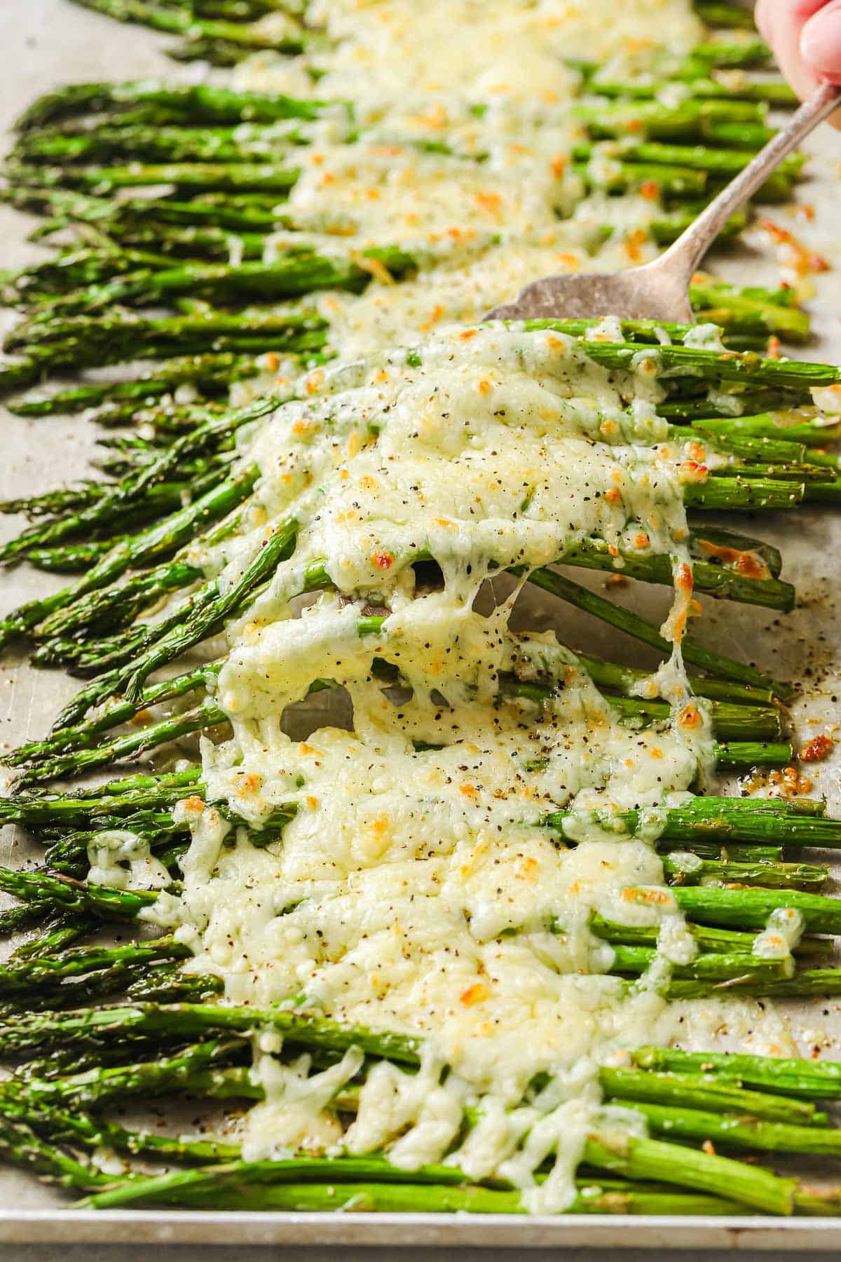 a baking sheet lined with parchment paper, full of roasted asparagus, garlic and melted cheese.