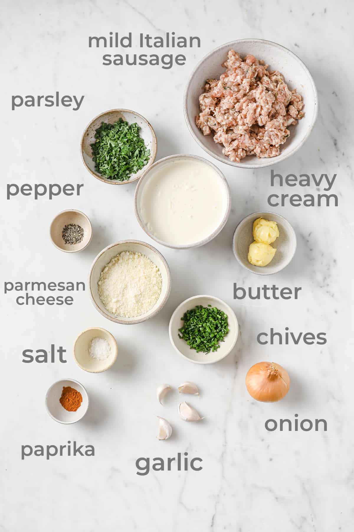 Ingredients all laid out to make sausage gravy - sausage, heavy cream, butter, garlic, herbs, salt, pepper, onion, and parmesan cheese.