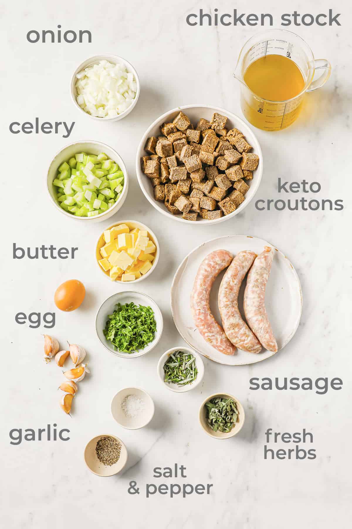 Ingredients all laid out to make stuffing - croutons, sausage, onion, celery, herbs, garlic, egg, and chicken stock.