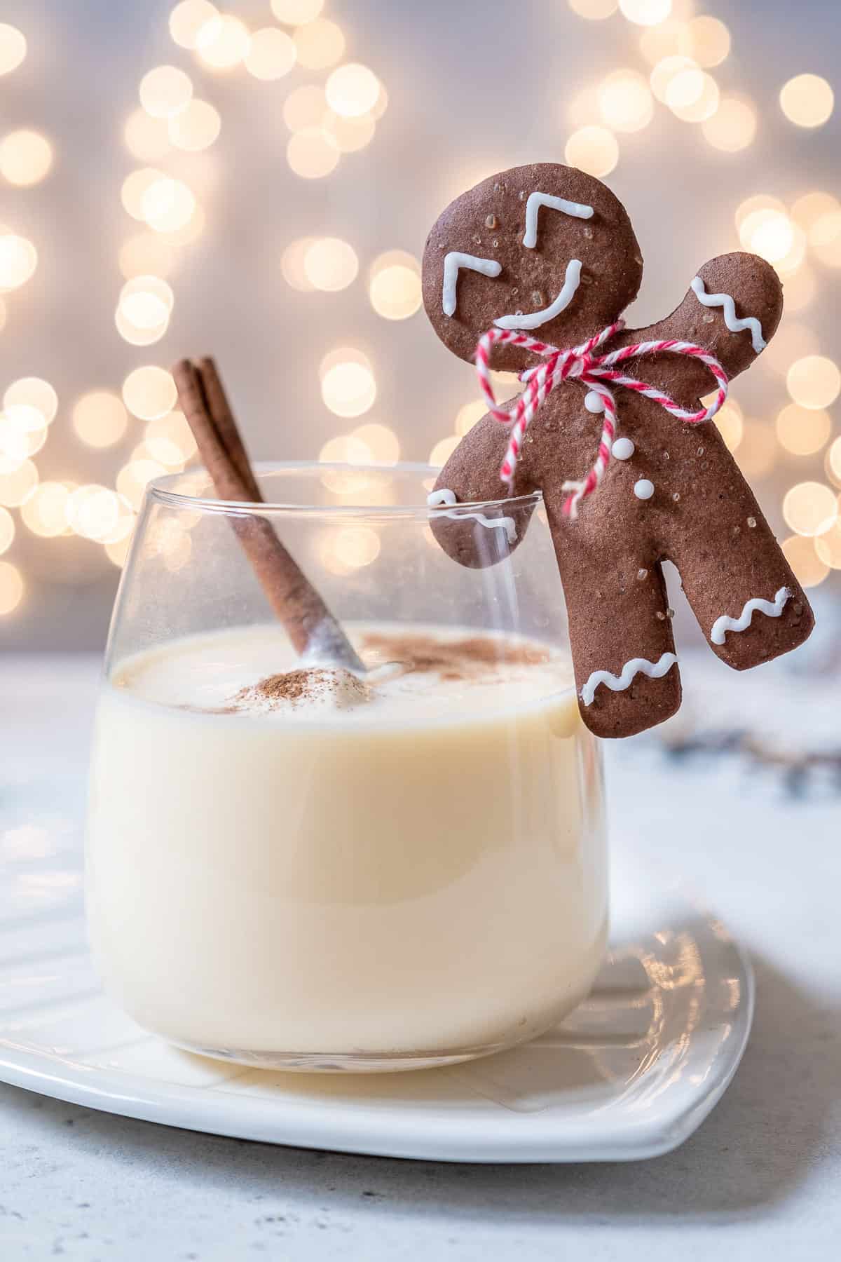 Two stemless wine glasses full of homemade eggnog, garnished with nutmeg, a cinnamon stick and a gingerbread man hanging off the side. 