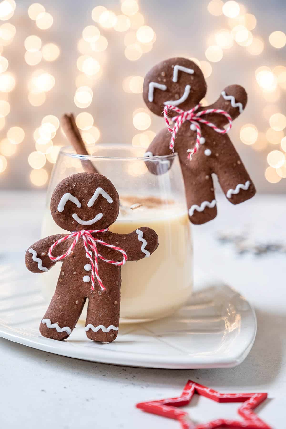 Two stemless wine glasses full of homemade eggnog, garnished with nutmeg, a cinnamon stick and a gingerbread man hanging off the side. 