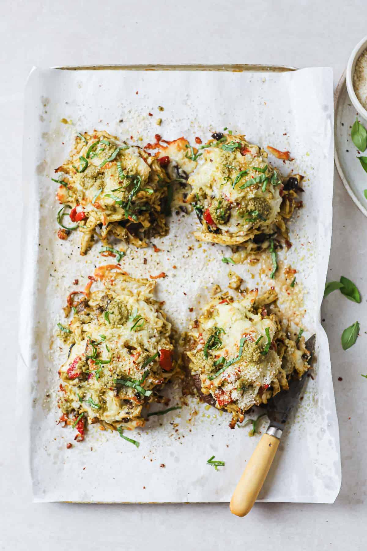 A parchment lined baking sheet with portobello mushrooms stuffed with chicken cheese, pesto, peppers, onions and garlic.