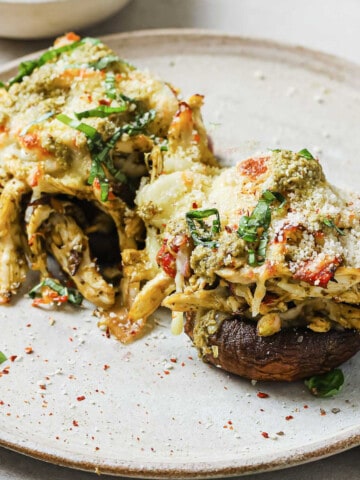 A plate with 2 portobello mushrooms stuffed with chicken, pesto, red peppers, cheese, garlic, and basil.