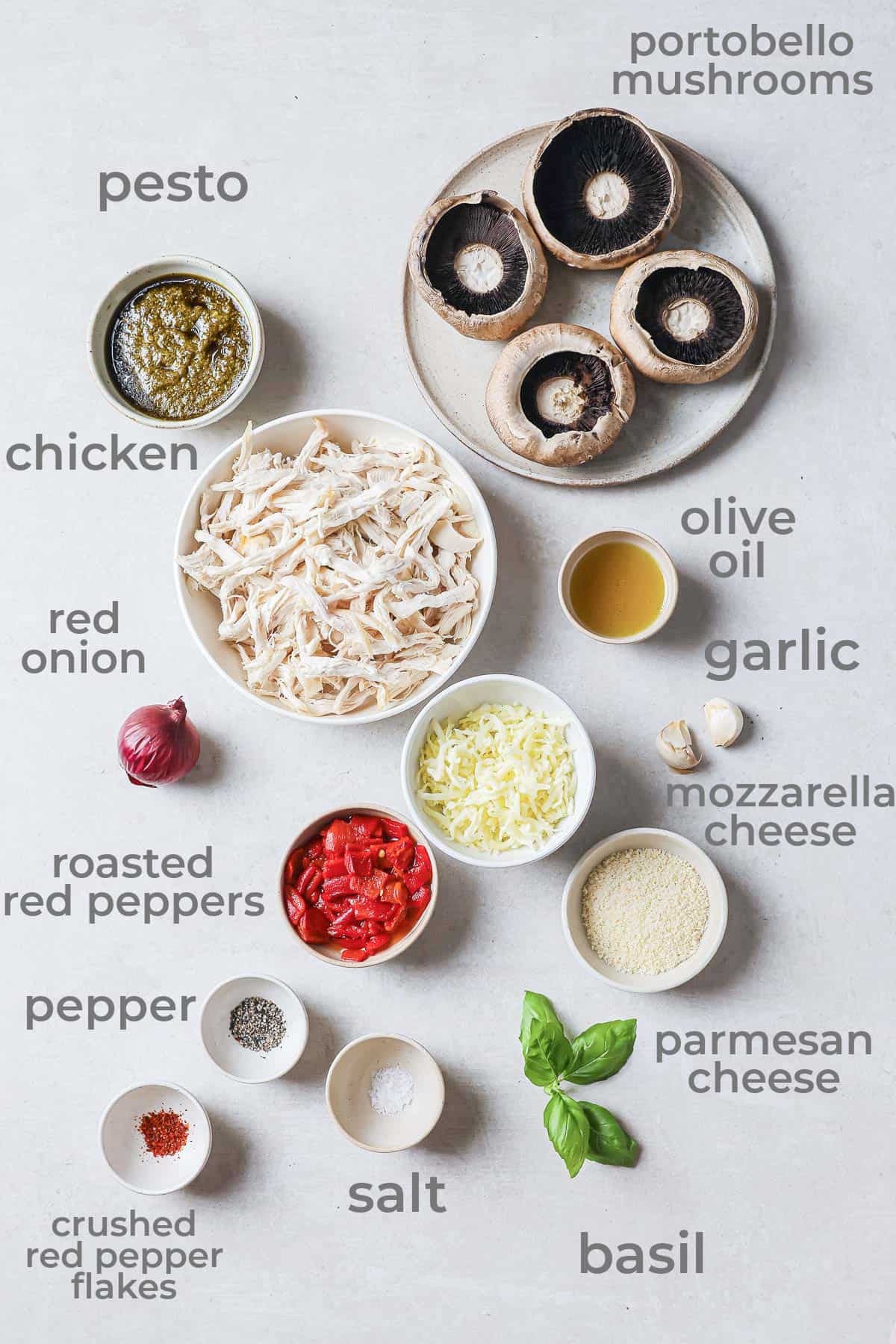 Ingredients all laid out to make stuffed mushrooms - portobello mushrooms, chicken, pesto, cheese, garlic, red peppers, basil, salt, and pepper.