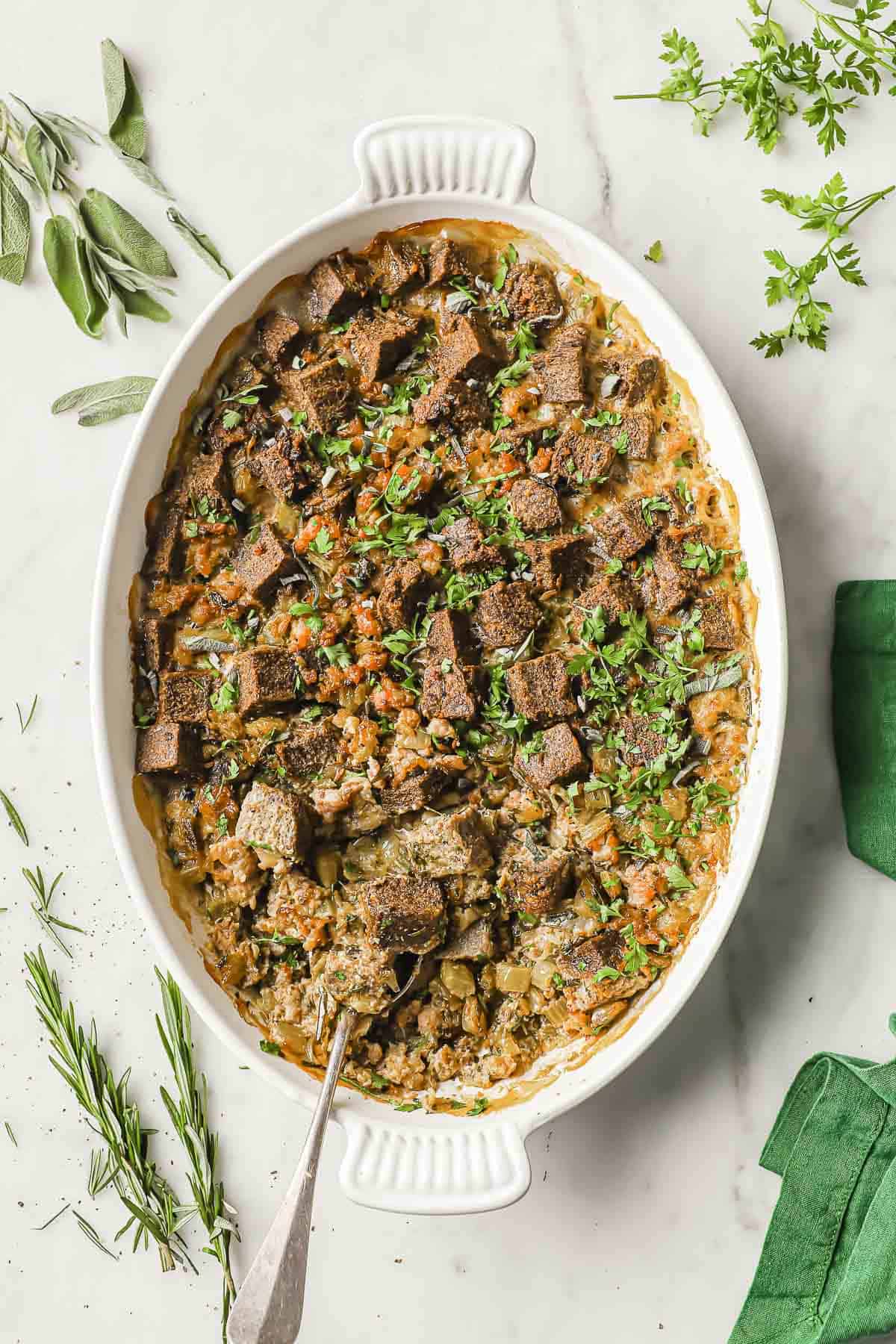 A white casserole dish full of low carb stuffing, made with keto bread, sausage, onion, celery and fresh herbs.