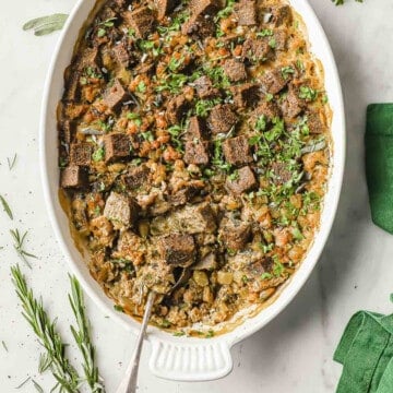 A white casserole dish full of low carb stuffing, made with keto bread, sausage, onion, celery and fresh herbs.