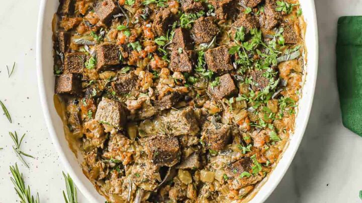 A white casserole dish full of low carb stuffing, made with keto bread, sausage, onion, celery and fresh herbs.
