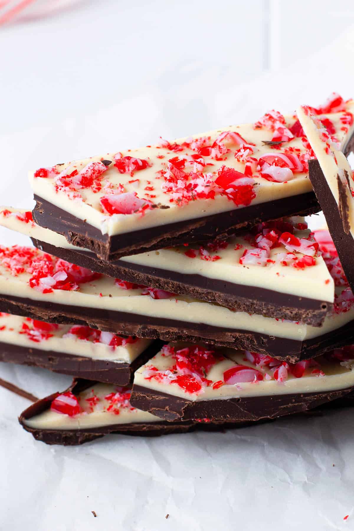 Peppermint bark made with white chocolate and dark chocolate, peppermint candies, broken up and served on white parchment paper.