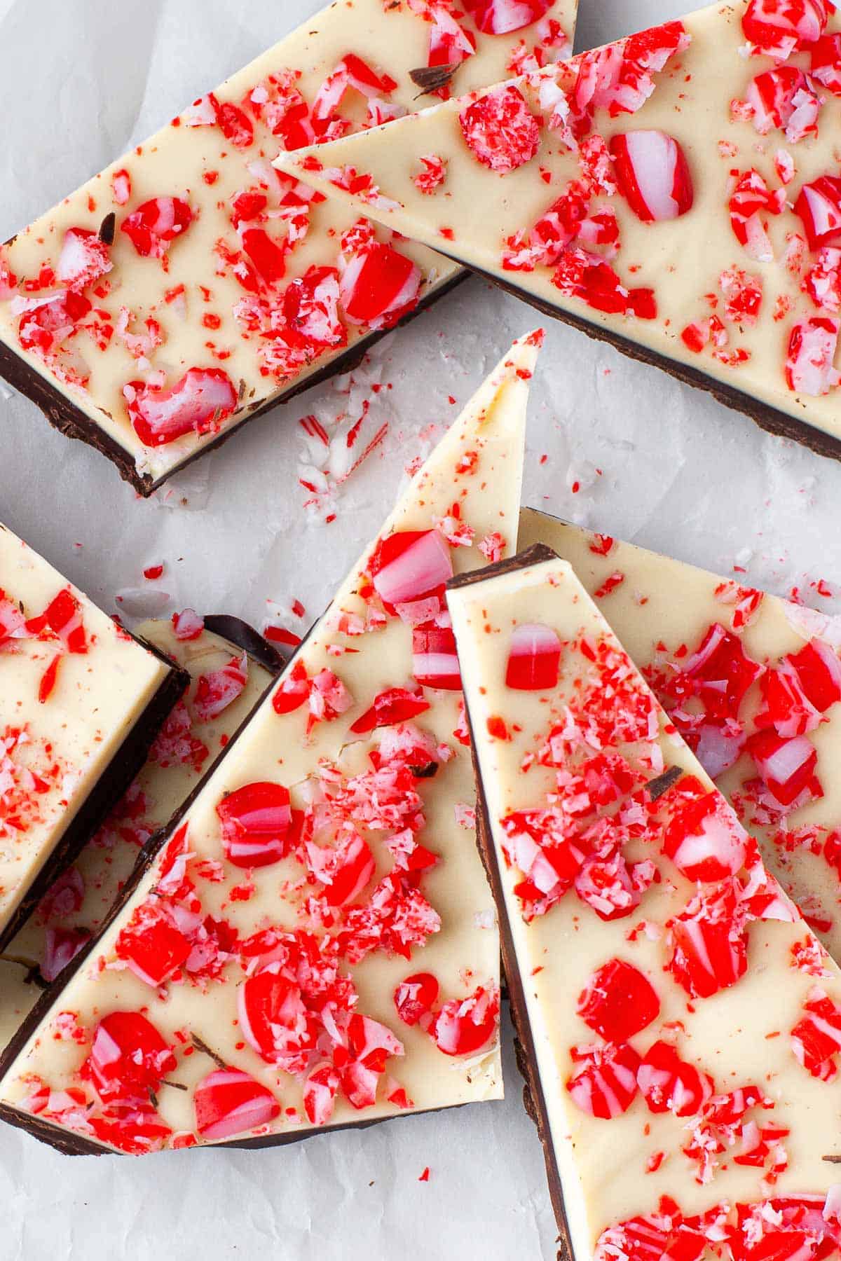 Peppermint bark made with white chocolate and dark chocolate, peppermint candies, broken up and served on white parchment paper. 