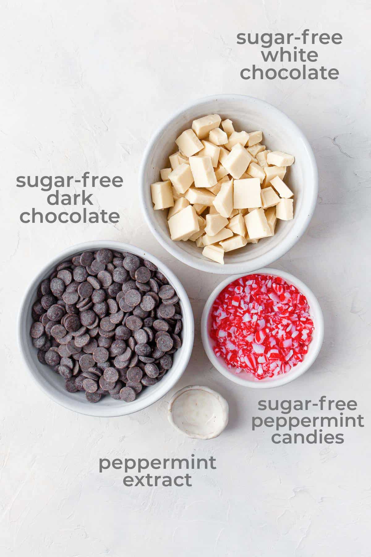 Ingredients laid out in individual bowls to make keto peppermint bark - white chocolate, dark chocolate, peppermint candies and peppermint extract.