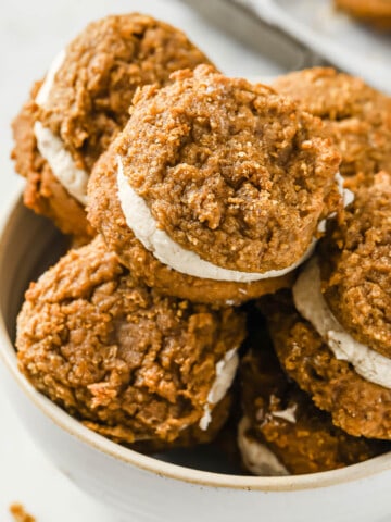 a dish lined with parchment paper and filled with pumpkin spice whoopie pies filled with cream cheese frosting.