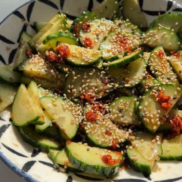 A decorative bowl full of cucumbers, soy sauce, rice vinegar, sesame seeds, chili past, garlic, and sweetener.