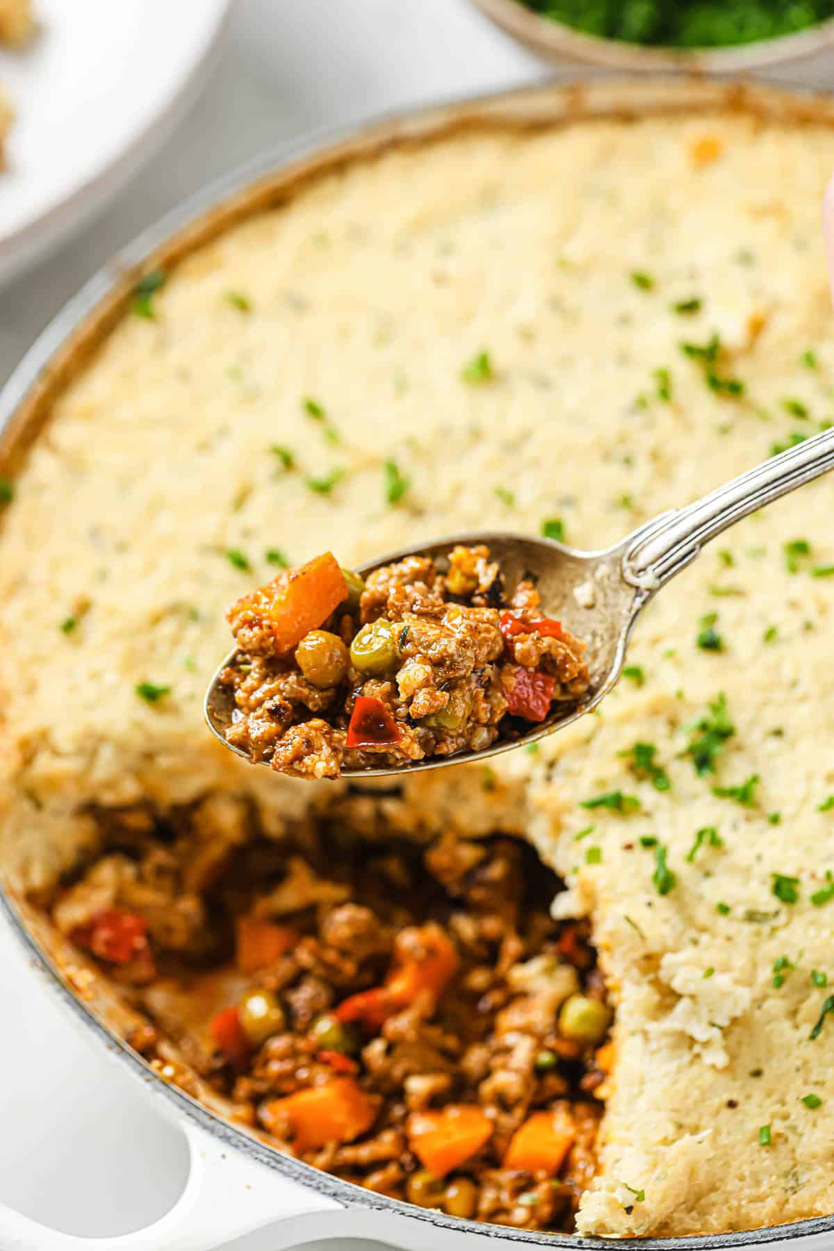An enameled cast iron skillet full of shepherds pie, made with beef, veggies, tomato sauce, and topped with cauliflower mash.