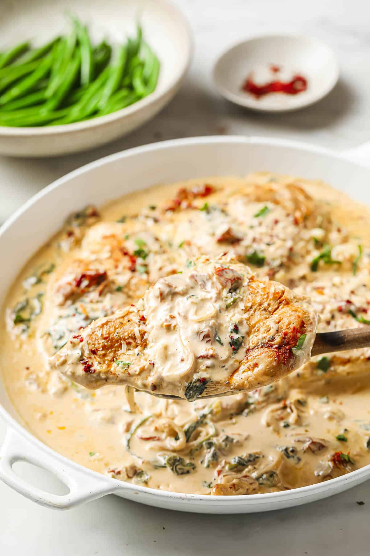 A white ceramic skillet full of a creamy chicken dish with chicken breasts, spinach, sun-dried tomatoes, garlic, onion, parmesan cheese and heavy cream.