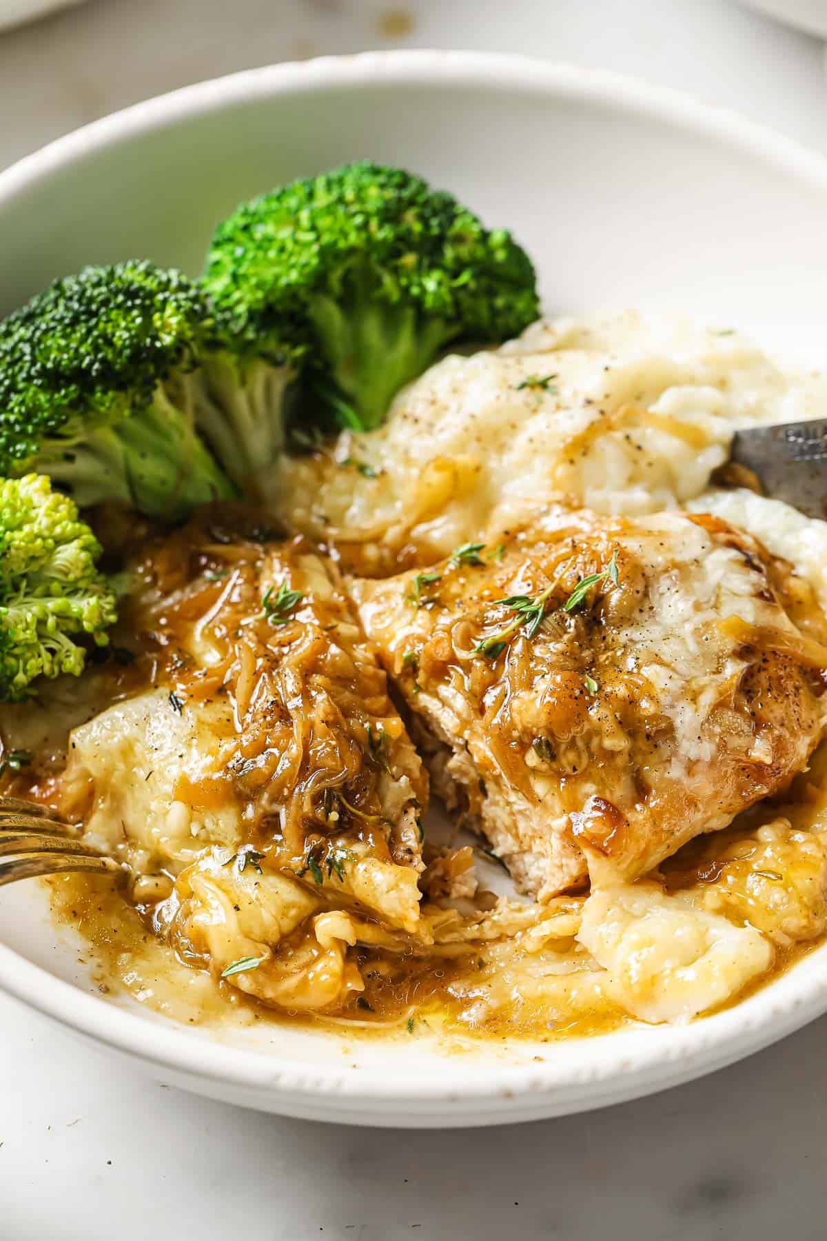 A serving bowl full of French onion chicken, on top of cauliflower mash, served with broccoli on the side. 