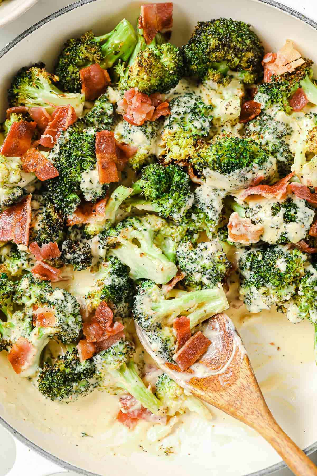 An enameled cast iron skillet with roasted broccoli, homemade cheese sauce and chopped crispy bacon.
