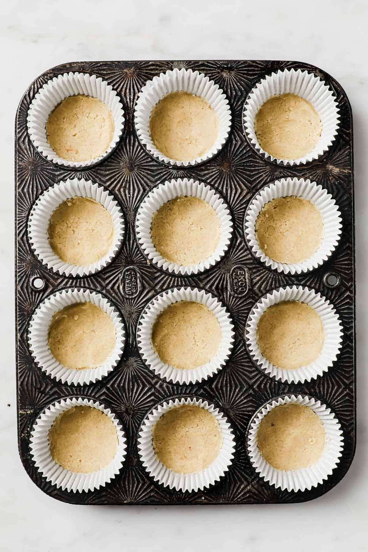 A muffin tin lined with muffin liners, filled with cheesecake batter, ready to be baked. 